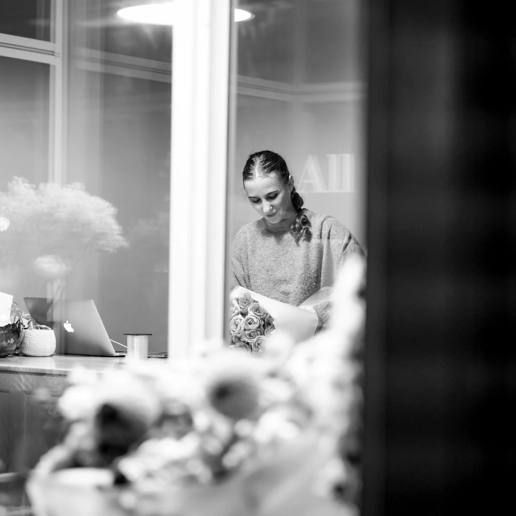 A neighborhood florist hand-arranges a seasonal bouquet at her wooden worktable.